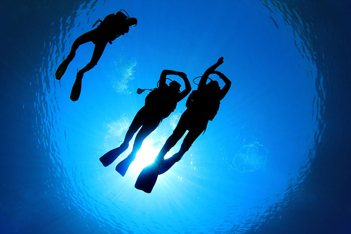 Three divers from shot from underneath with sky above